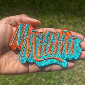 May include: Two embroidered patches with the word "Miami" in orange lettering on a teal background.