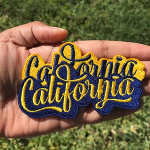 May include: A blue and yellow embroidered patch with the word "California" written in a stylized font.