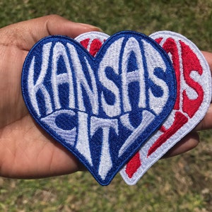 May include: Two heart-shaped embroidered patches, one blue with white lettering that says "KANSAS CITY" and one red with white lettering that says "KANSAS".