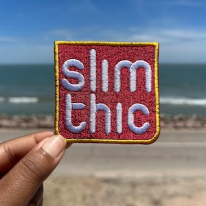 May include: A red square patch with a yellow border. The patch has white embroidered text that reads "slim thic".