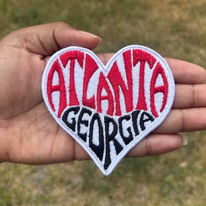 May include: White heart-shaped patch with red embroidered text "ATLANTA" and black embroidered text "GEORGIA".