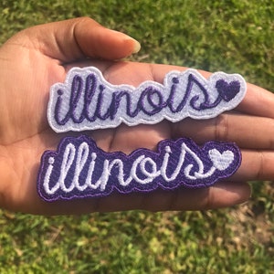 May include: Two white iron-on patches with purple outlines. Both patches say "Illinois" with a small white heart to the right of the word.