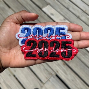 May include: Two iron-on patches with the text "2025 Senior" in white cursive lettering. The top patch is blue with white outlining. The bottom patch is red with black outlining.
