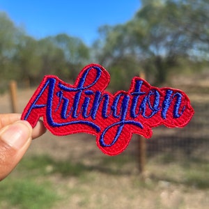 May include: Red felt patch with blue embroidered lettering that reads "Arlington".