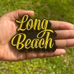 May include: A black embroidered patch with yellow stitching that says "Long Beach".