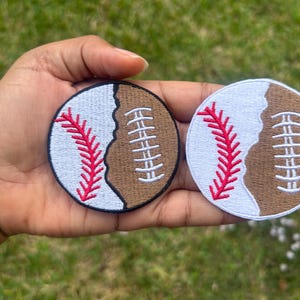 May include: Two embroidered iron-on patches, one with a baseball and the other with a football, both with white stitching and red stitching. The patches are on a brown background.