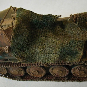 May include: A detailed model of a military tank, painted in shades of brown and green, with a camouflage net draped over the top. The number "321" is visible on the side. The tank has multiple wheels and tracks, showcasing a realistic design.
