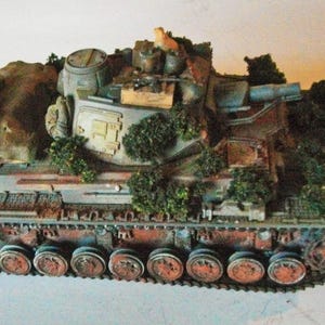 May include: A detailed model tank with a camouflage design, featuring a mix of green, brown, and gray colors. The tank has visible tracks, a turret, and is adorned with miniature foliage, creating a realistic, battle-worn appearance.