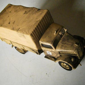 May include: A detailed model of a vintage truck, featuring a tan canvas-covered cargo bed and a weathered, brown cab. The truck has black tires and a detailed front grill, evoking a sense of history and nostalgia.