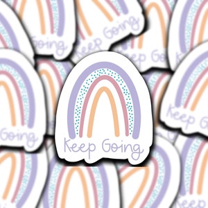 May include: A sticker featuring a pastel rainbow design with the words "Keep Going" in a handwritten font. The rainbow has layers of purple, pink, and peach colors, with a dotted blue accent. The sticker is white with a black outline.