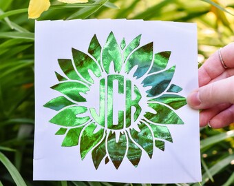 Könnte beinhalten: Ein grüner, schimmernder Vinyl-Aufkleber mit einer Sonnenblume und dem Monogramm "JCB" in der Mitte.