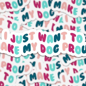 May include: A sticker with the text "I just want to make my dog proud" in pink, teal, and dark blue lettering on a white background.