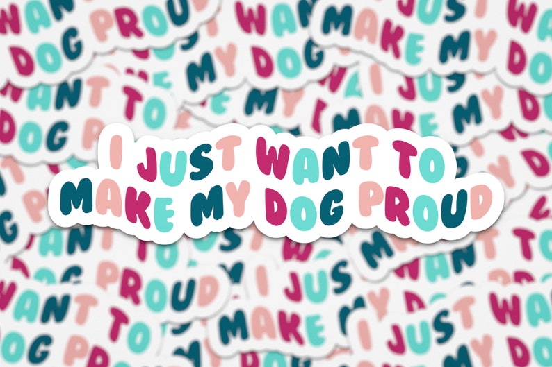 May include: A sticker with the text "I just want to make my dog proud" in pink, teal, and dark blue lettering on a white background.