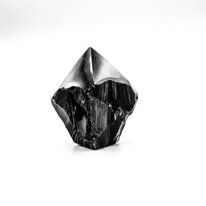 May include: A black obsidian crystal point with a rough, textured surface.