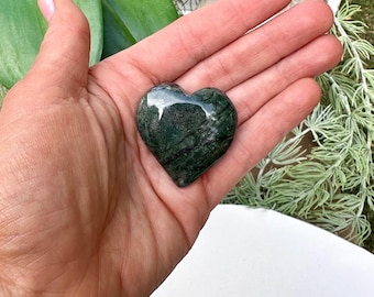 May include: A green heart-shaped stone with dark green and white streaks. The stone is polished and smooth.