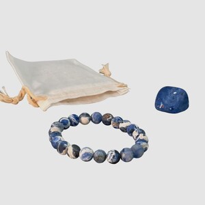 May include: A blue and white gemstone bracelet with a matching blue gemstone and a white drawstring bag.