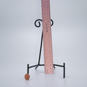 May include: A black metal display stand with three legs and a curved top. The stand is 38 cm tall and is used to display small objects, such as plates or figurines.