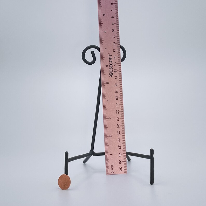 May include: A black metal display stand with three legs and a curved top. The stand is 38 cm tall and is used to display small objects, such as plates or figurines.