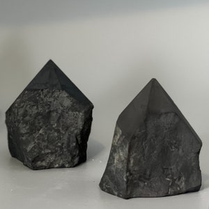 May include: Two black, rough-textured, crystal-shaped objects. The objects are made of a dark, opaque material and have a pointed top.