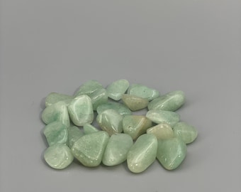 May include: A collection of smooth, light green tumbled stones. The stones are various sizes and shapes, with a polished, glossy finish.