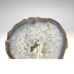 May include: Two agate bookends. Each bookend is a half-circle shape with a gray and white interior and a brown and tan outer edge. The bookends are cut to create a flat surface for standing upright.