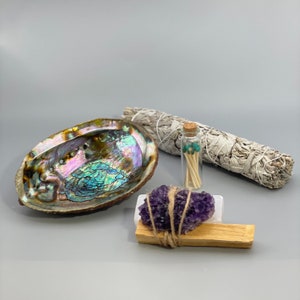 May include: A set of smudging tools including a white sage bundle, abalone shell, amethyst crystal, and a small glass bottle of matches.