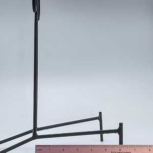 May include: Black metal easel stand with two legs and a curved top. The stand is approximately 18 cm wide.