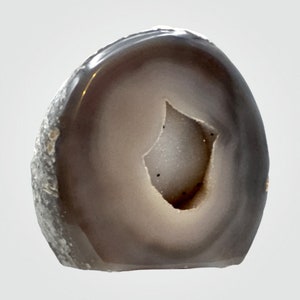 May include: A gray and white agate geode with a large opening in the center. The geode is polished and has a smooth surface.