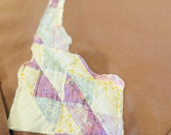 Könnte beinhalten: Ein altrosa Sweatshirt mit einem Applikation in Form des Bundesstaates Idaho. Die Applikation besteht aus Patchwork-Stoffen in Lila, Gelb und Weiß, wodurch ein einzigartiges, handgefertigtes Design entsteht. Ein bequemes, lässiges Kleidungsstück.