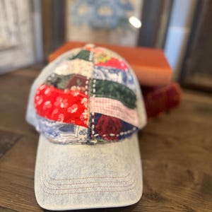 May include: A denim baseball cap with a patchwork design on the crown. The patchwork features various fabrics in red, blue, green, and pink. The brim is a light blue denim with a curved shape.