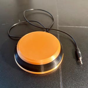 May include: Orange and black foot switch with a black cable and a 1/4 inch (6.35 mm) audio jack. The round switch has an orange top and a black base. The cable is connected to the side of the switch.