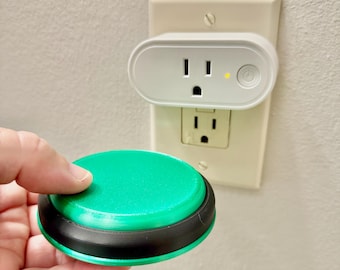 Peut inclure: Un bouton rond vert et noir tenu devant une prise murale blanche. Au-dessus de la prise se trouve une prise intelligente blanche avec un bouton d'alimentation et un petit voyant jaune, branchée sur la prise supérieure de la plaque murale.