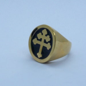 May include: A gold ring with a black enamel center featuring a stylized cross design.