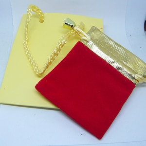 May include: A red velvet drawstring pouch with a gold trim and a gold cord. The pouch is sitting on a yellow surface.