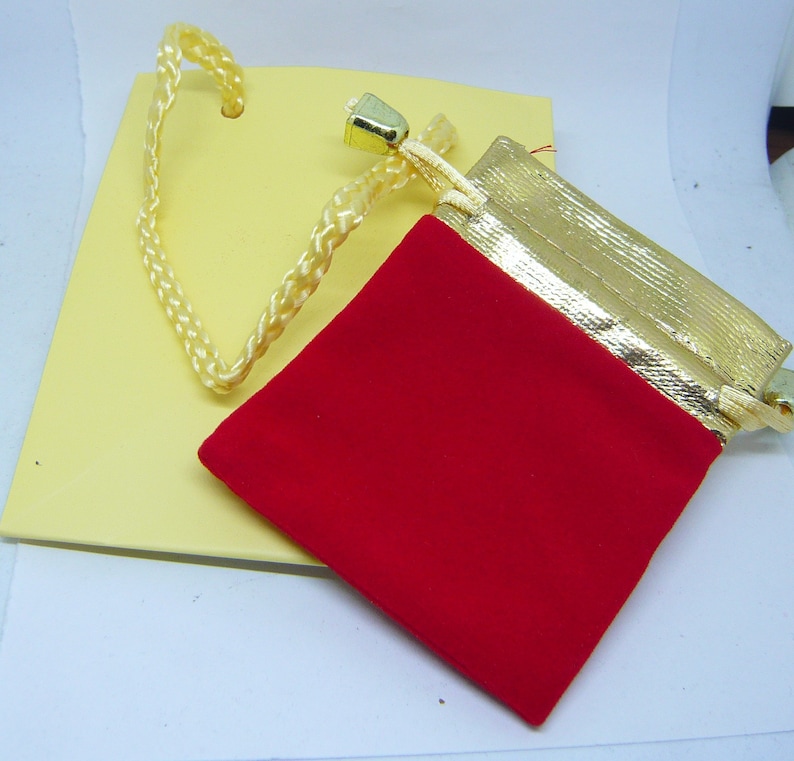 May include: A red velvet drawstring pouch with a gold trim and a gold cord. The pouch is sitting on a yellow surface.