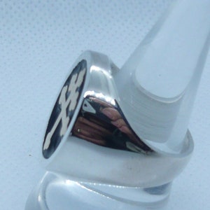 May include: A silver ring with a black oval inlay featuring a white cross design.