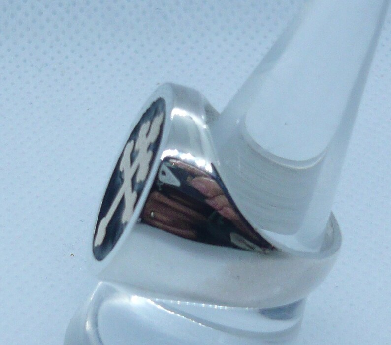 May include: A silver ring with a black oval inlay featuring a white cross design.