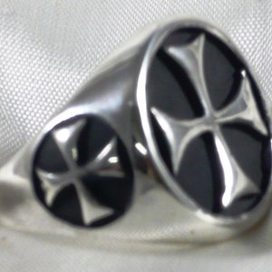 Könnte beinhalten: Ein silberner Ring mit einem schwarzen Onyxstein, der mit einem silbernen Kreuz verziert ist.