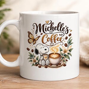 May include: A white ceramic mug featuring a graphic illustration of a cartoon dog holding a small cup next to a larger coffee cup. The text Michelle's Coffee is printed in brown script above the dog, surrounded by a butterfly, flowers, and coffee beans.