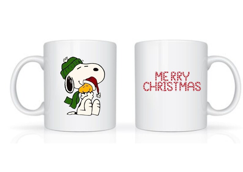 Może przedstawiać: Biały ceramiczny kubek z Snoopy w zielonej czapce i szaliku oraz czapce Świętego Mikołaja, trzymający ż&oacute;łtego ptaka. Druga strona kubka ma czerwony napis "MERRY CHRISTMAS".