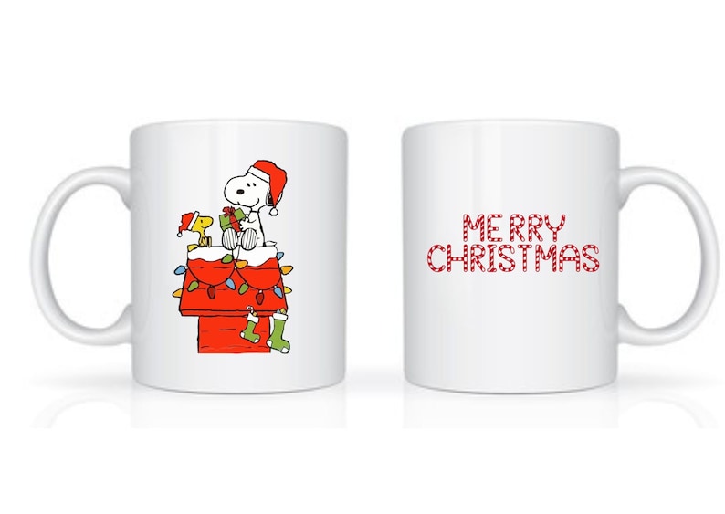 Może przedstawiać: Biały ceramiczny kubek z świątecznym wzorem. Z jednej strony Snoopy i Woodstock w czapkach Świętego Mikołaja na czerwonej budzie ozdobionej lampkami i skarpetami. Z drugiej strony napis "MERRY CHRISTMAS" w kolorze czerwonym.