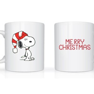 Może przedstawiać: Biały ceramiczny kubek z Snoopy w czerwono-białej czapce świątecznej w paski. Na kubku widnieje r&oacute;wnież napis "MERRY CHRISTMAS" w czerwonych, świątecznych literach. Idealny prezent świąteczny.