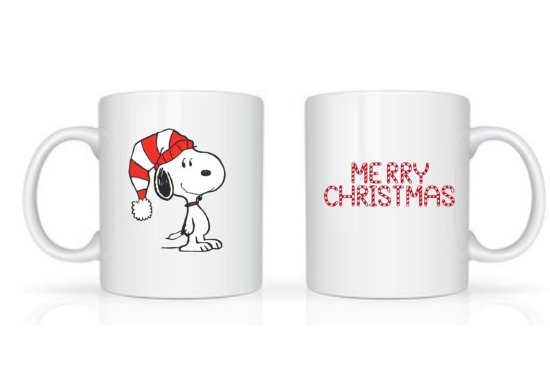 Może przedstawiać: Biały ceramiczny kubek z Snoopy w czerwono-białej czapce świątecznej w paski. Na kubku widnieje r&oacute;wnież napis "MERRY CHRISTMAS" w czerwonych, świątecznych literach. Idealny prezent świąteczny.