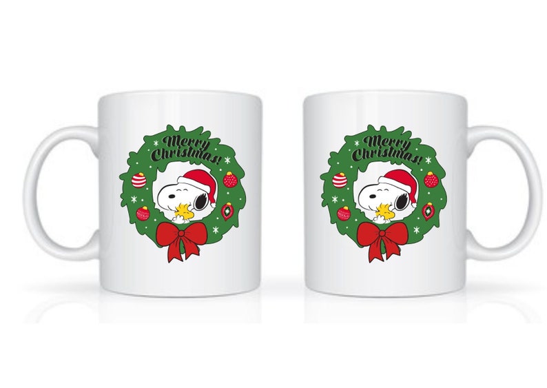 Może przedstawiać: Biały ceramiczny kubek z Snoopy w czapce Świętego Mikołaja, otoczony zielonym wieńcem z czerwonymi ozdobami i czerwoną kokardą. Tekst "Merry Christmas!" jest wyświetlany nad Snoopy. Świąteczny, świąteczny design.