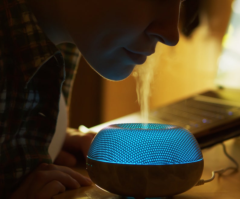 Puede incluir: Una persona inhala el vapor de un difusor de aceites esenciales azul y gris con un patr&oacute;n de panal en la parte superior.