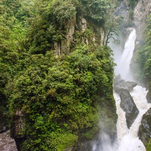 Puede incluir: Una cascada verde y exuberante cae por un acantilado rocoso, rodeada de una densa vegetaci&oacute;n tropical. El agua es blanca y espumosa, creando una neblina.