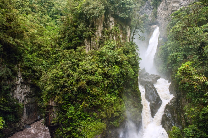 Puede incluir: Una cascada verde y exuberante cae por un acantilado rocoso, rodeada de una densa vegetaci&oacute;n tropical. El agua es blanca y espumosa, creando una neblina.