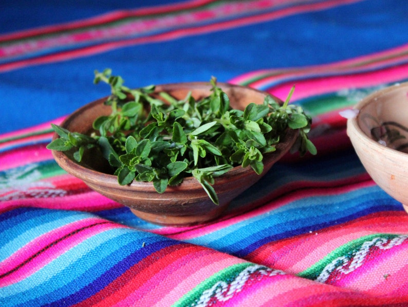 Puede incluir: Un cuenco de madera lleno de hierbas verdes frescas, sentado sobre una tela de rayas de colores.