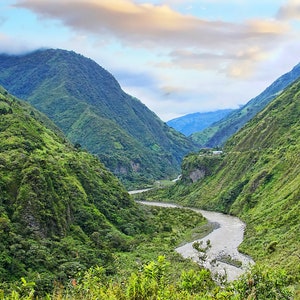 Puede incluir: Un r&iacute;o sinuoso fluye a trav&eacute;s de un valle verde y exuberante rodeado de monta&ntilde;as boscosas y empinadas. El cielo es de un azul suave con nubes blancas tenues.