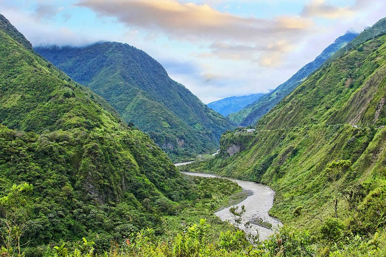 Puede incluir: Un r&iacute;o sinuoso fluye a trav&eacute;s de un valle verde y exuberante rodeado de monta&ntilde;as boscosas y empinadas. El cielo es de un azul suave con nubes blancas tenues.